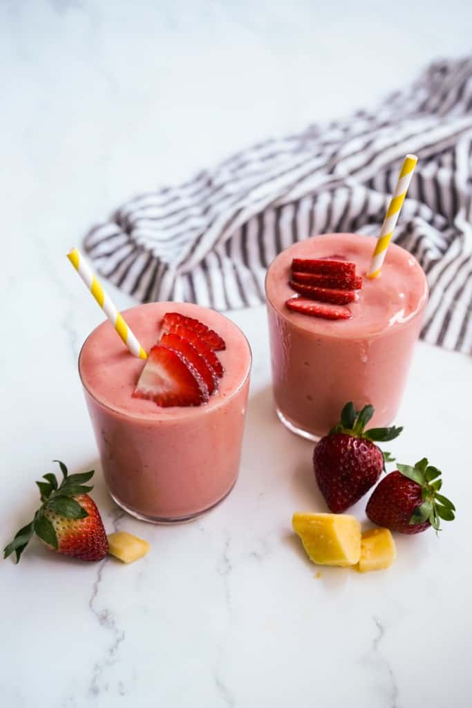 Two glasses mango strawberry smoothies with straws in it