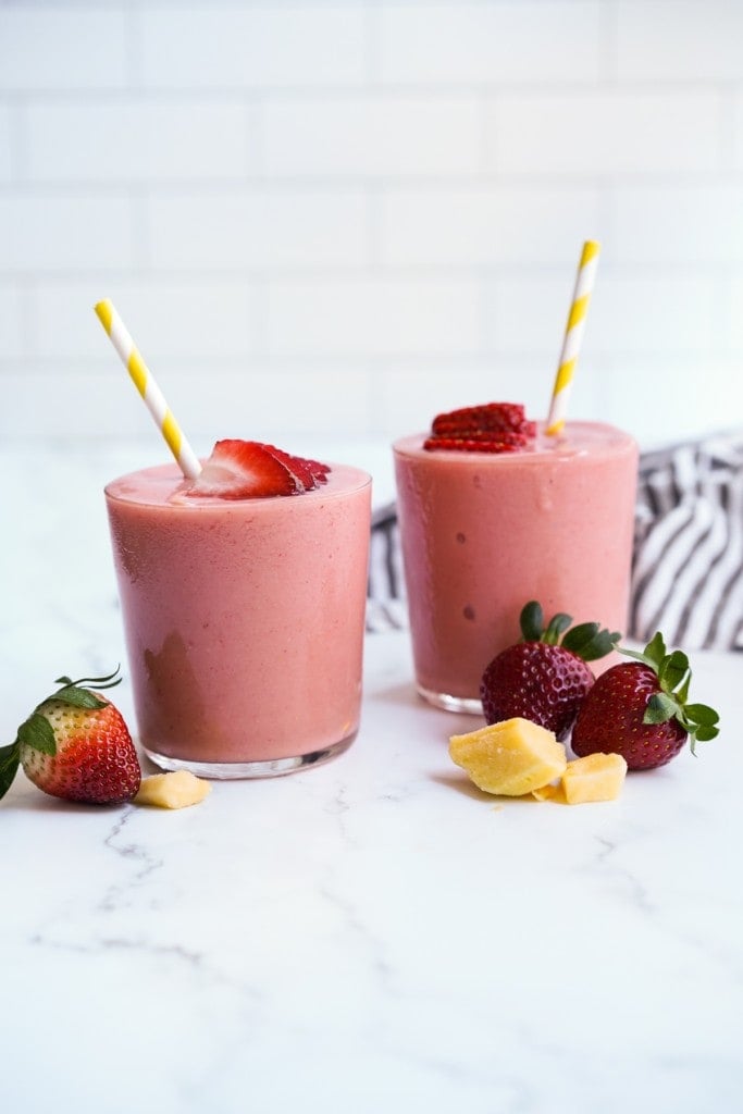 Two glasses of pink smoothie with strawberry slices on top
