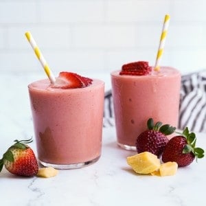 Two glasses of mango strawberry smoothie with mango and strawberry slices around them