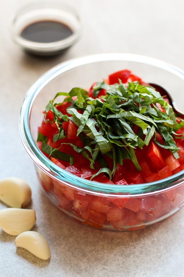 Kuutioidut tuoreet tomaatit, tuoretta basilikaa, oliiviöljyä, valkosipulia, suolaa ja pippuria kulhossa