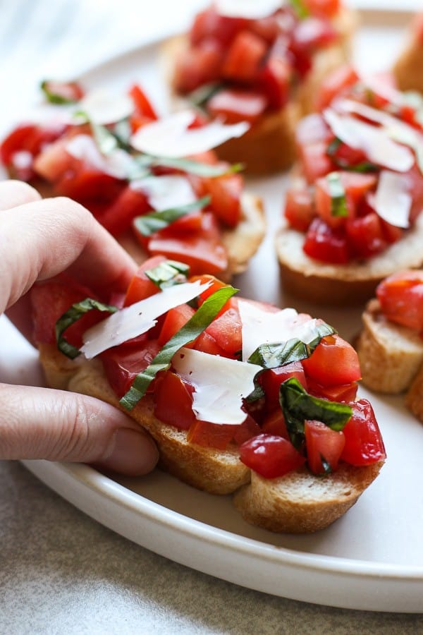 Die Hand greift nach einem Stück Bruschetta mit Tomaten, Basilikum und Balsamico-Essig