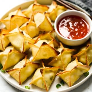 Baked Cream Cheese Rangoons stacked together on a plate with sweet chili dipping sauce
