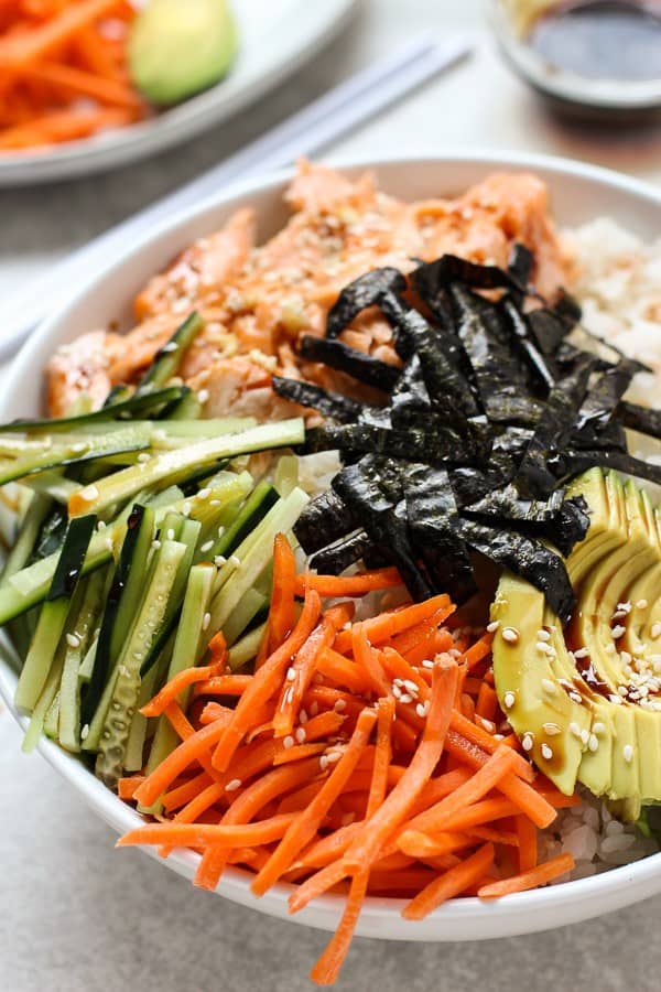 A bowl of Deconstructed Baked Salmon Sushi Bowl topped with avocados, seaweed, carrots and cucumber