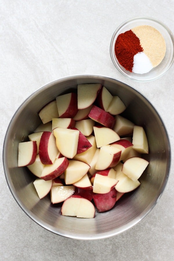 A bowl of uncooked diced red potatoes with a small bowl of spices for Roasted Garlic Parmesan Potatoes