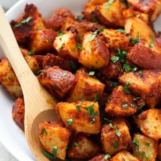 Using a wooden spoon to spoon out some Roasted Garlic Parmesan Potatoes from a bowl