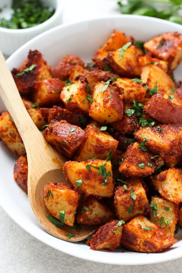 Using a wooden spoon to spoon out some Roasted Garlic Parmesan Potatoes from a bowl