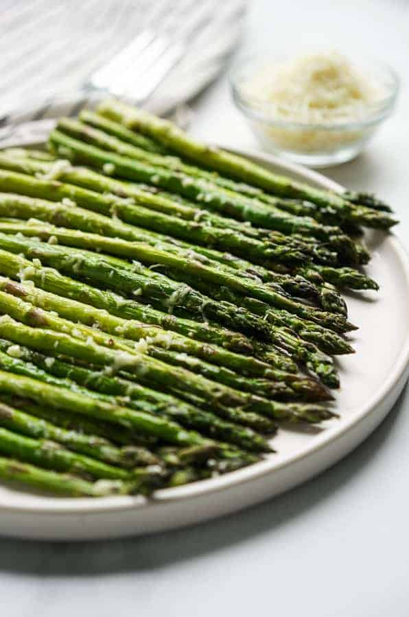 A plate of Easy Garlic Parmesan Asparagus with a small bowl of parmesan cheese in the background