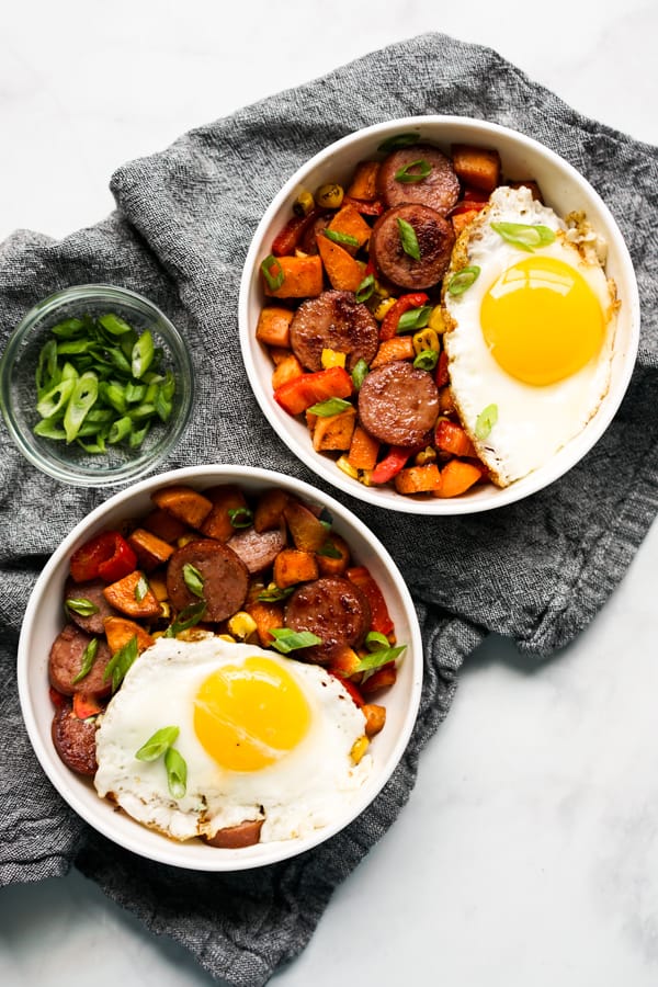 Two bowls of Sweet Potato and Kielbasa Breakfast Hash with sunny side up eggs on top