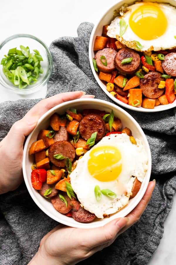 Hand grabbing a bowl of Sweet Potato and Kielbasa Breakfast Hash