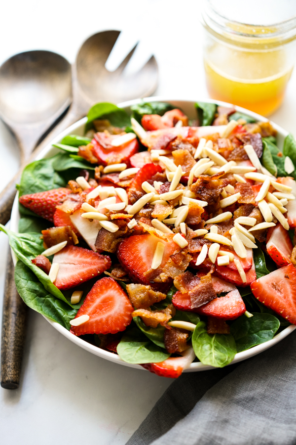 A bowl of Strawberry Bacon Spinach Salad with Lemon Maple Dressing on the side