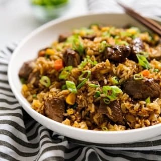 A bowl of fried rice with steaks with a pair of chopsticks on the bowl