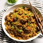 A bowl of Steak Fried Rice with kitchen towel tucked underneath and a pair of chopsticks on it