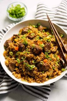 A bowl of Steak Fried Rice with kitchen towel tucked underneath and a pair of chopsticks on it