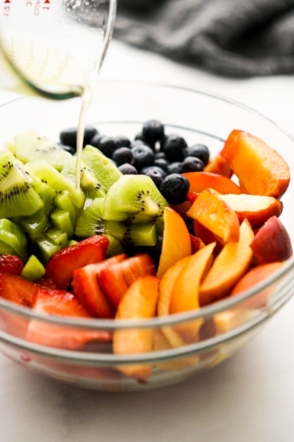 Pouring Honey Lime Dressing onto a bowl of fruit salad