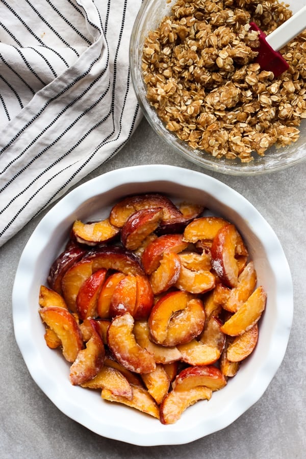 Fresh peaches in a round pan with a bowl of crumble on the side