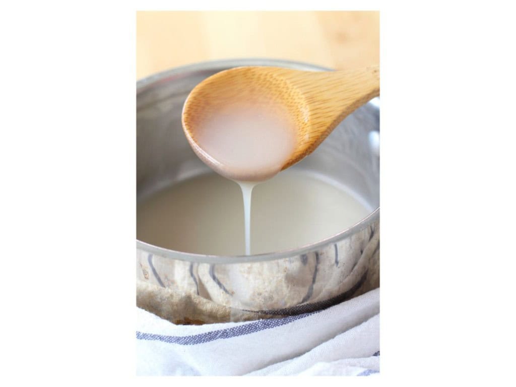 A wooden spoon is used to pick up creamy coconut sauce from a pot
