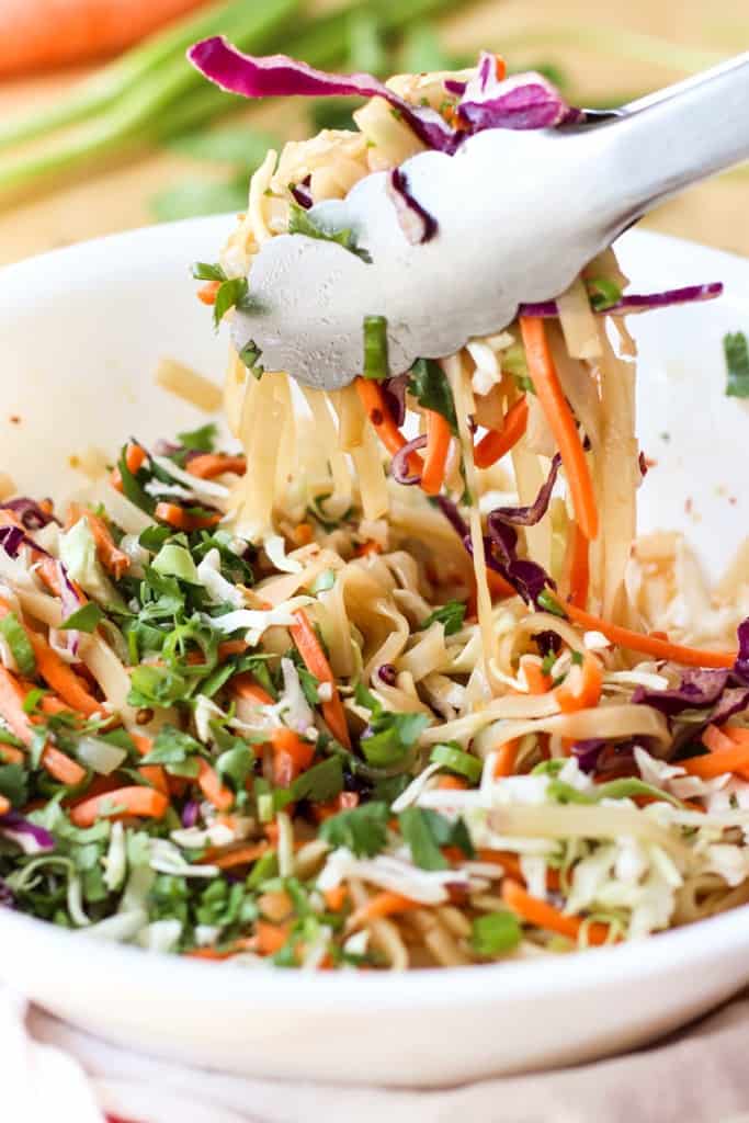 Tossing thai noodle bowl with a pair of tongs