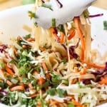 Using a pair of tossing to toss Thai noodles with cabbage and carrots in sauce