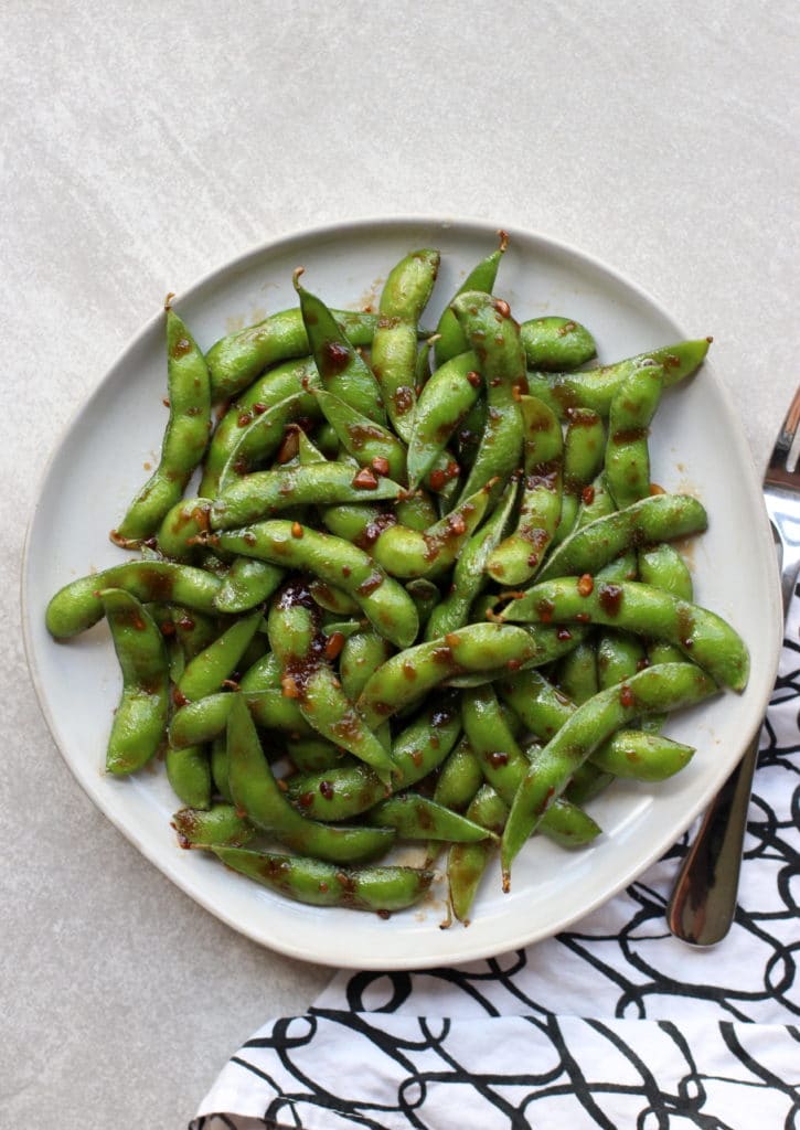 Top down view of a plate of Garlic Edamame coated in soy sauce and garlic pieces