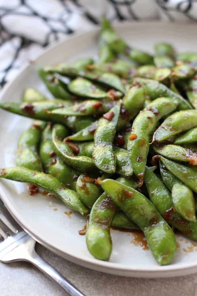 Sticky Garlic Edamame on a plate with fork on the side