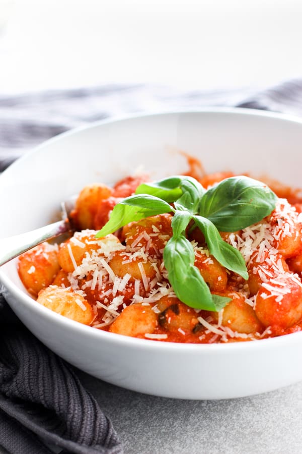 A bowl of Tomato Basil Gnocchi topped with fresh basil and with a fork in it