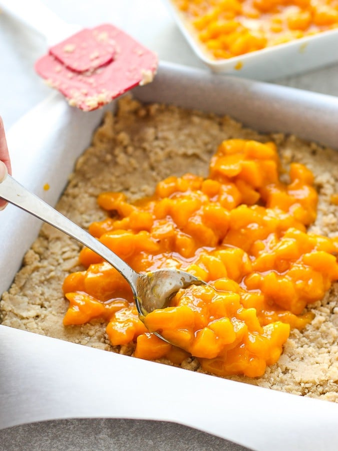 Spreading mango filling onto crumble