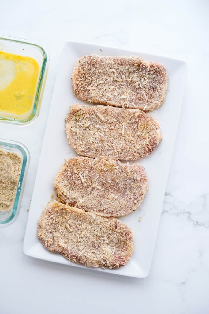 uncooked breaded pork chops lined up on a rectangular plate