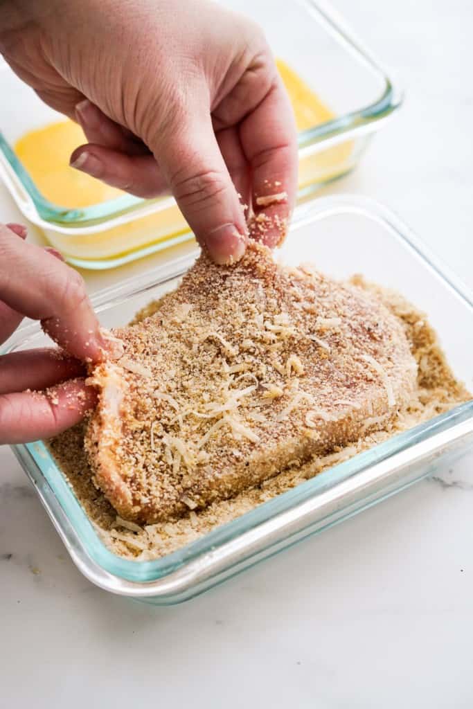 Breading a piece of pork chops with breadcrumbs and grated parmesan