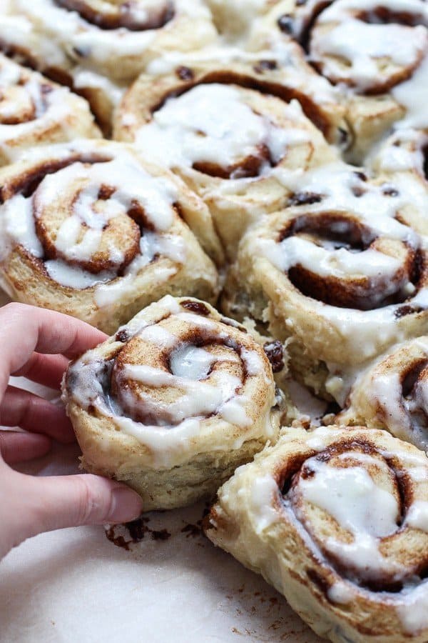 Hand grabbing a cinnamon roll topped with sweet icing
