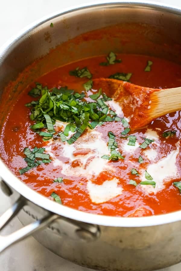 Adding fresh basil and heavy cream to a pot of tomato soup