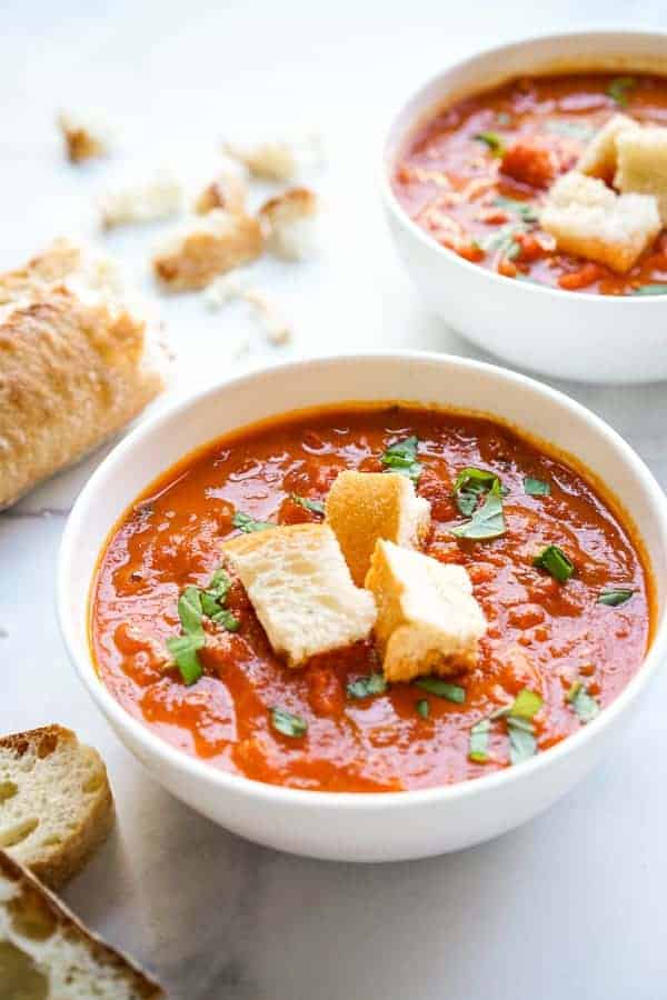 Two bowls Simple Tomato Soup topped with croutons and fresh basil