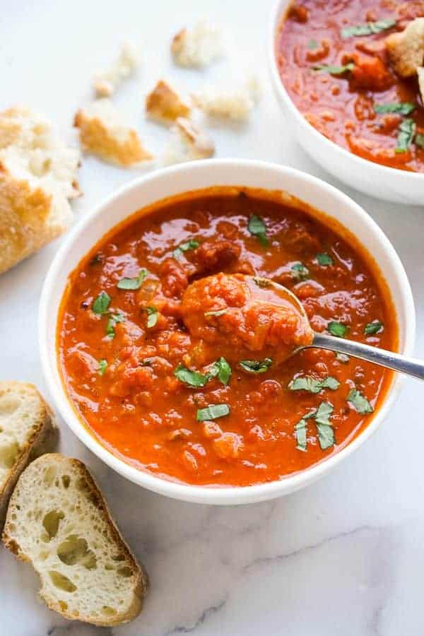 Using a spoon to dig into a bowl of Tomato Soup with chunks of canned tomatoes