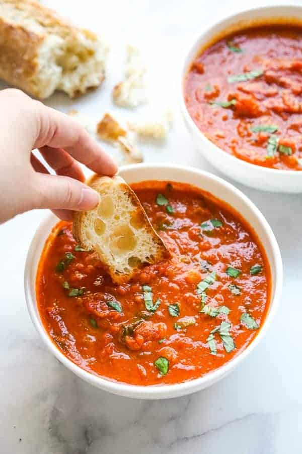 Dipping baguette into a bowl of tomato basil soup made with canned tomatoes
