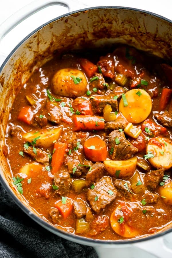 A pot of thick beef stew with carrots, potatoes and tomatoes