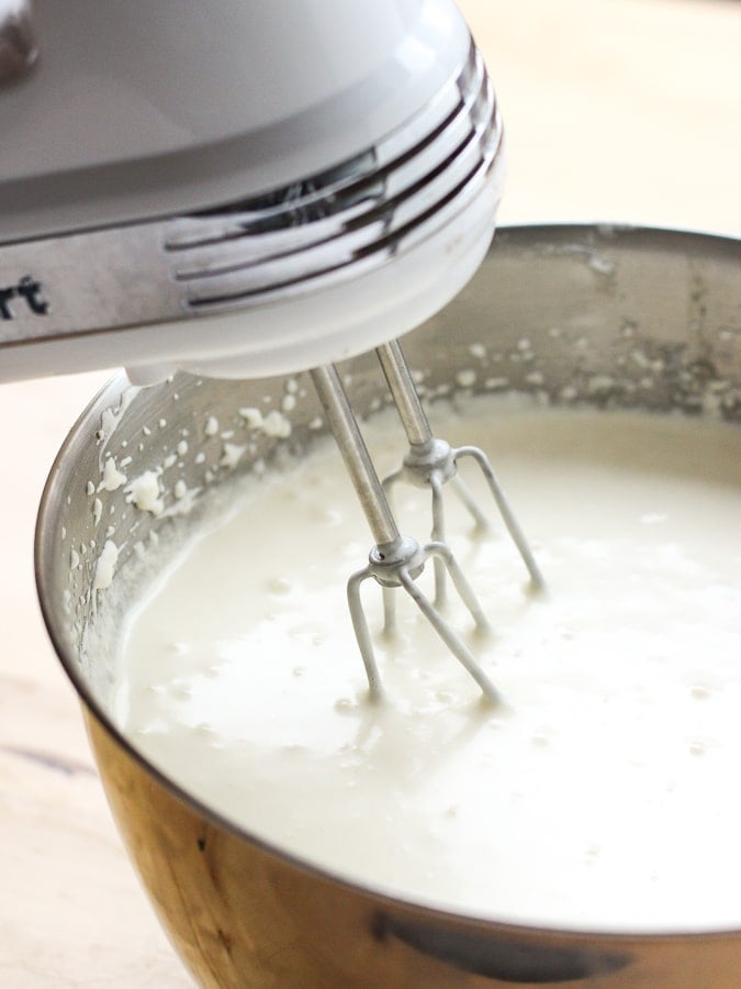 whisking cheesecake filling in a large bowl with a hand electric mixer