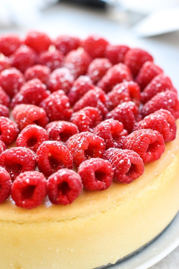 A whole cheesecake without crust topped with raspberries and powdered sugar