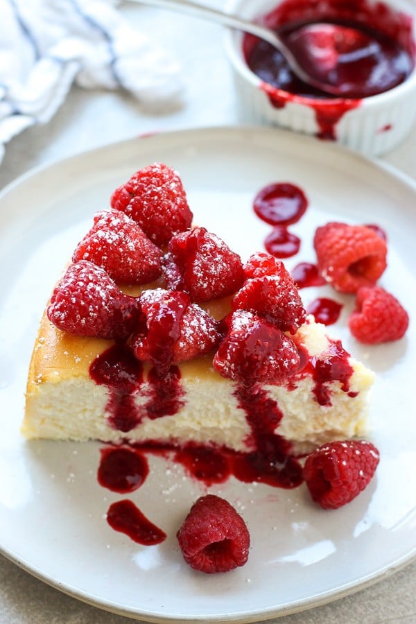 A slice of Italian ricotta cheesecake on a plate topped with raspberries and raspberry sauce