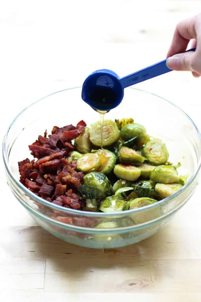Drizzling honey into a bowl of roasted Brussels sprouts and bacon pieces