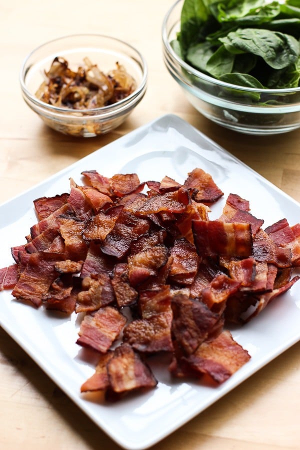 A plate of bacon, along with bowls of caramelized onions and spinach