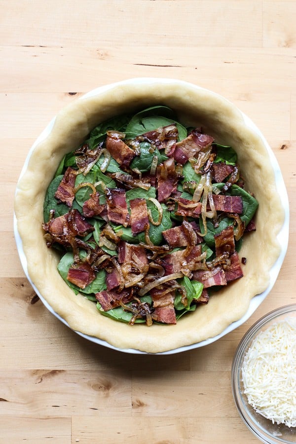 Unbaked pie crust with bacon, caramelized onions and spinach in it. 