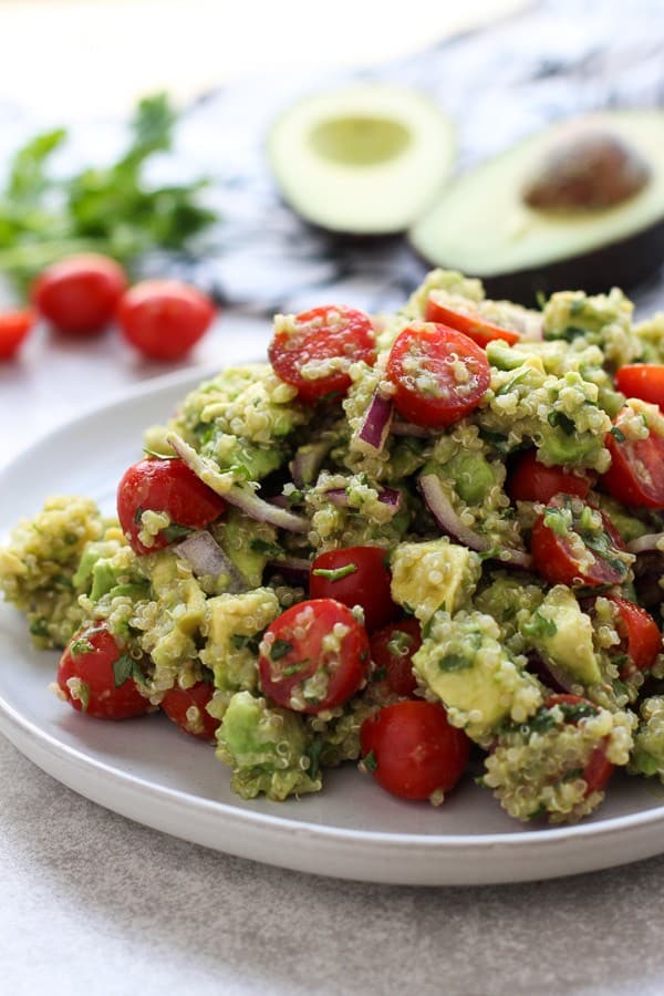 A plate of Avocado Quinoa Salad with avocados and tomatoes in the background