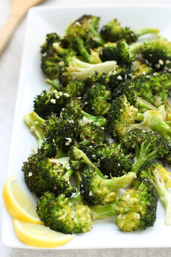 A rectangular plate of roasted broccoli with lemons