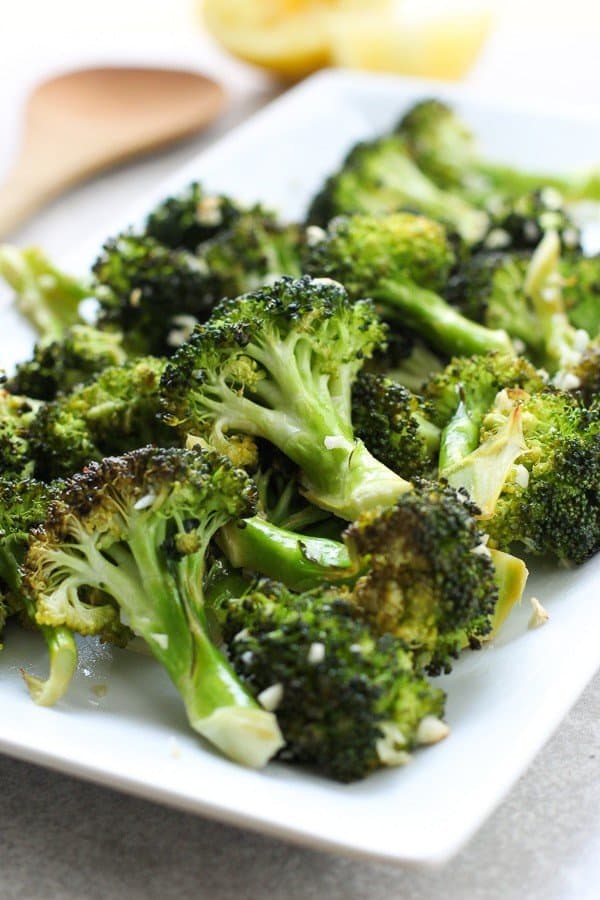 Roasted Lemon Garlic Broccoli on a rectangular plate with lemons behind