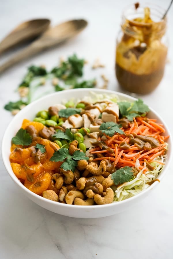 A bowl of Asian salad with shredded cabbage, carrots and cashews with peanut dressing in the background