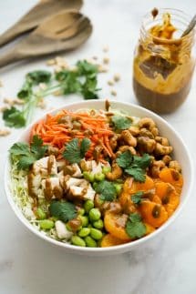 Asian Peanut Chicken Salad ingredients in a large bowl with peanut dressing and spatulas in the background