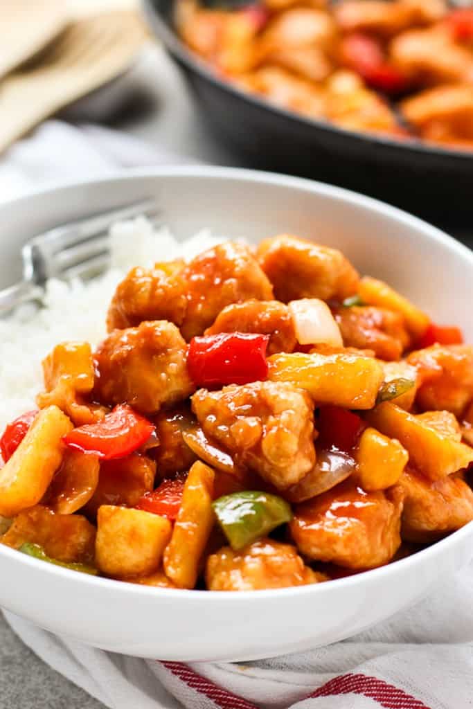 A bowl of sweet and sour chicken on top of rice, fork on the side