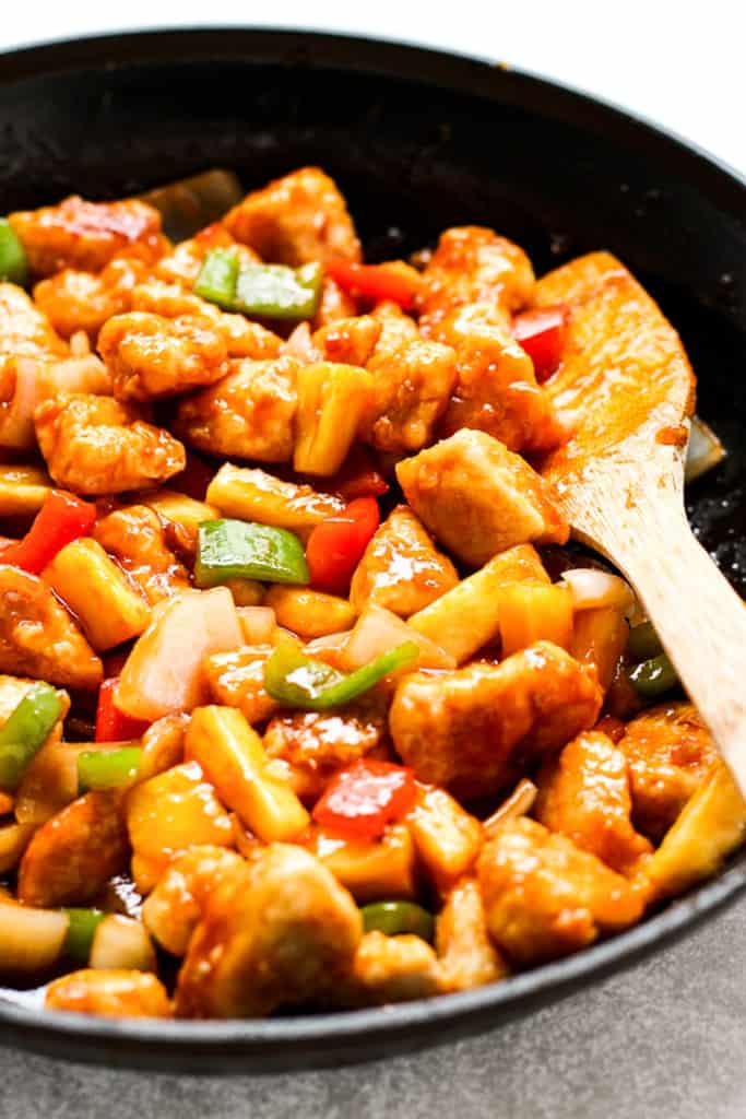 Sweet and sour chicken along with bell peppers and pineapple in a skillet