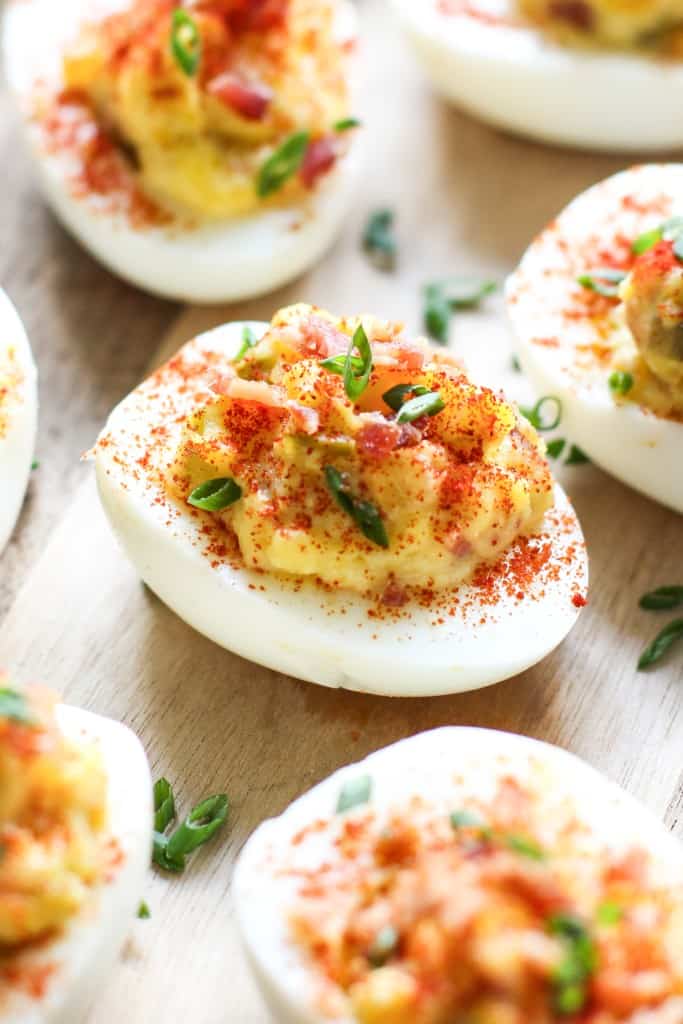 Close up on a bacon deviled egg topped with chives and dusted with smoked paprika.