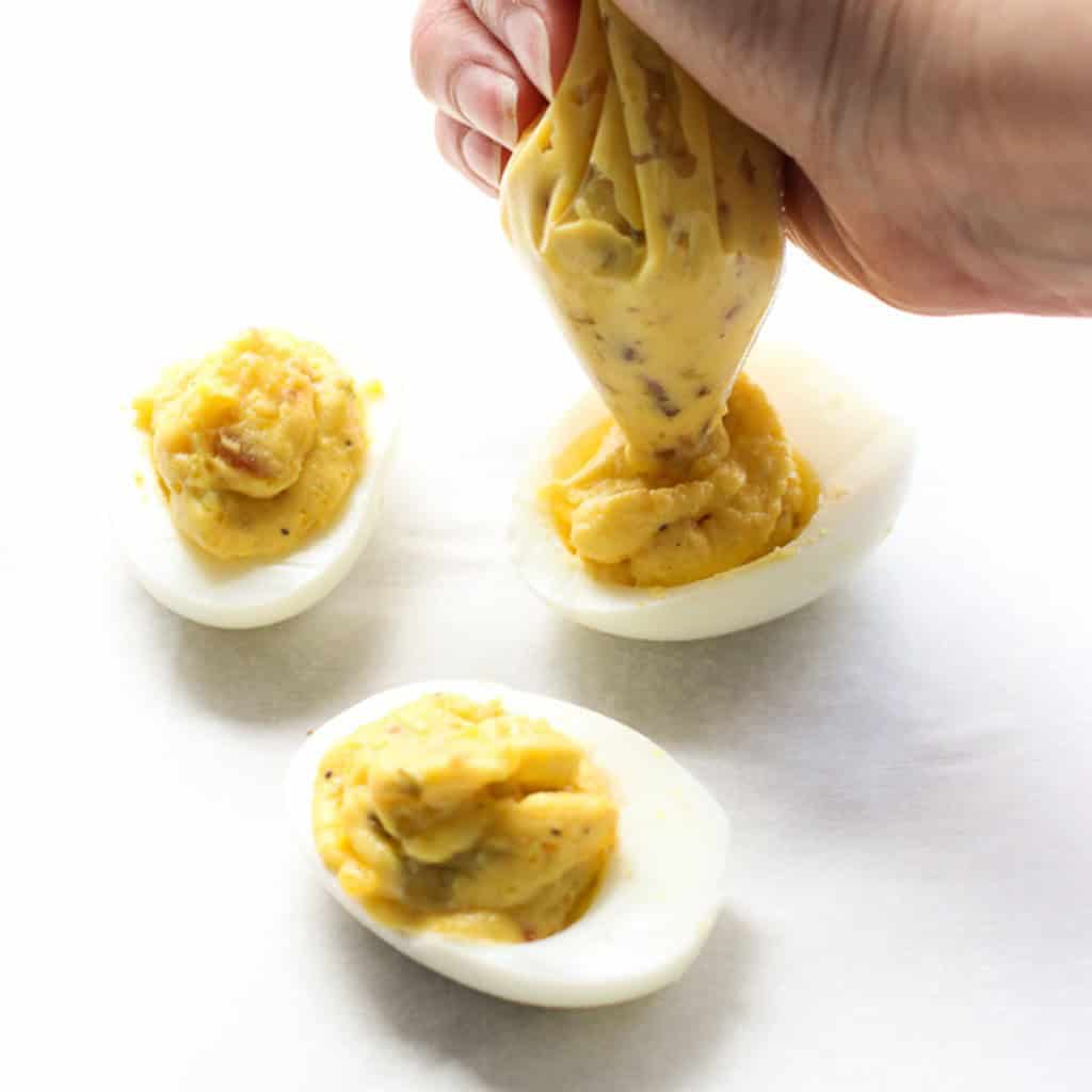 Pipping a sliced-in-half boiled egg white with egg yolk mixture