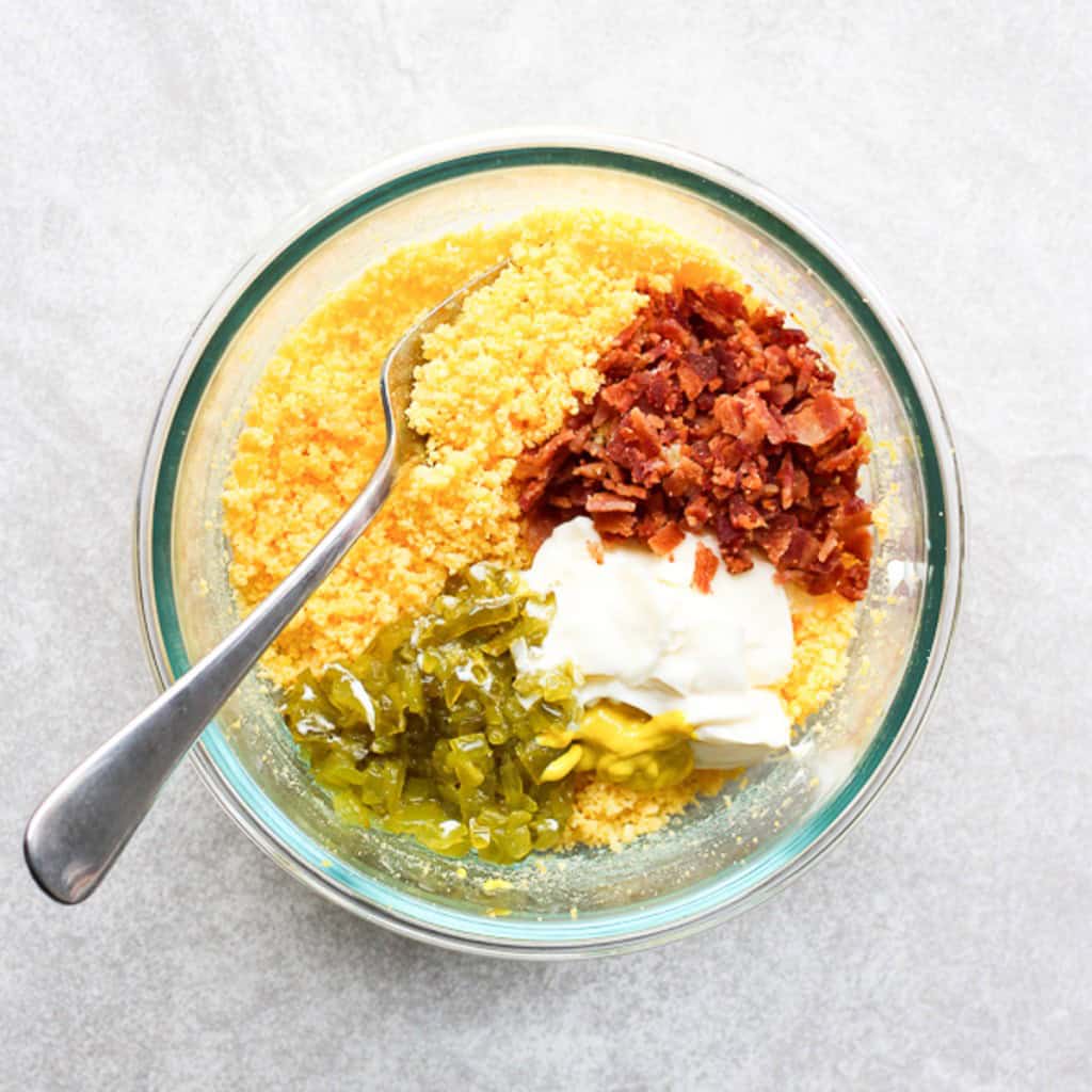 Mashed up egg yolk, bacon crumbles, mayonnaise, pickle relish in a bowl
